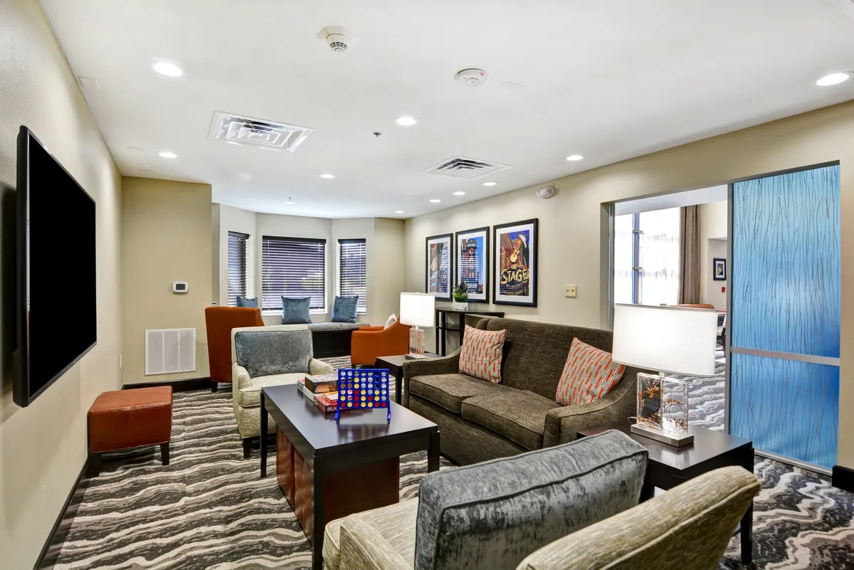 A bright living area with a modern sofa adorned with decorative cushions, a coffee table with colorful accents, a wall-mounted TV, vibrant artwork on the walls, and a distinctive blue sliding door. The space exudes comfort and individuality.