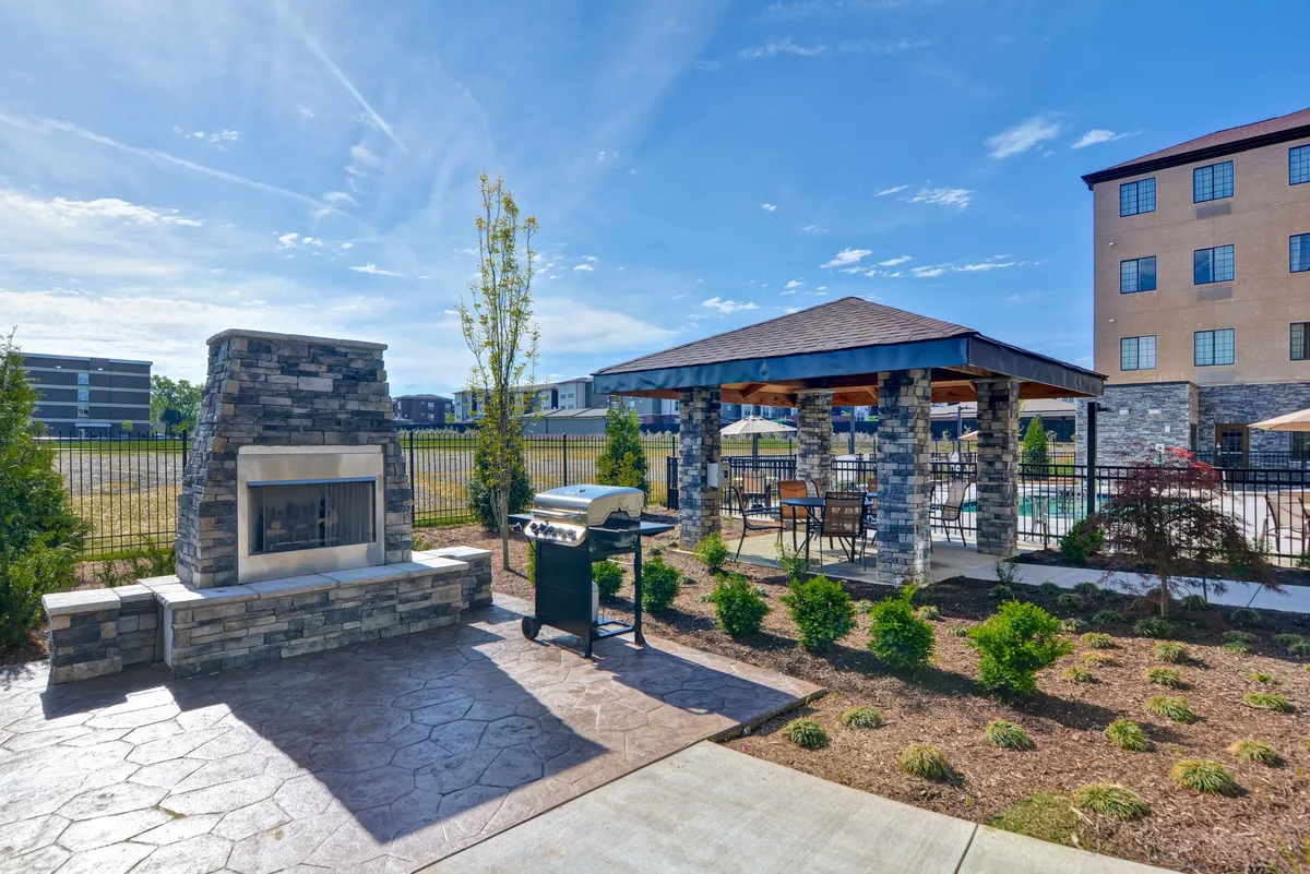 A welcoming outdoor space featuring a fireplace, grill, a gazebo, and beautifully landscaped gardens. The area is designed for barbecuing, relaxing, and enjoying social gatherings, with comfortable seating that encourages guests to unwind after shopping or dining.