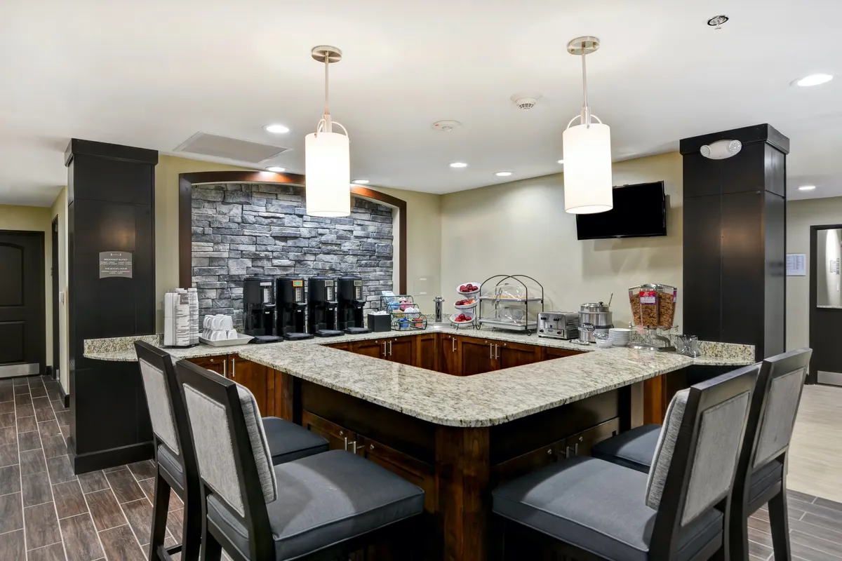 This image highlights a social coffee station with a granite countertop, decorative stone wall, and a relaxed seating area for guests. The scene suggests a spot for morning conversations, afternoon snacks, or networking with fellow travelers.