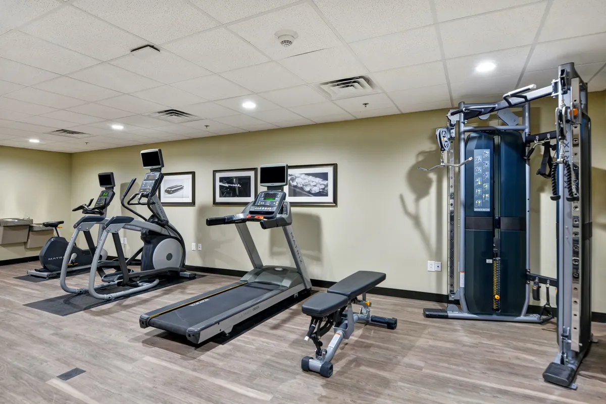 A bright, well-equipped fitness center featuring a treadmill, elliptical machine, weight bench, and a multigym machine. The space is clean and modern, with plenty of natural light and ample room for guests to enjoy a focused workout. The variety of equipment supports both cardio and strength training routines.